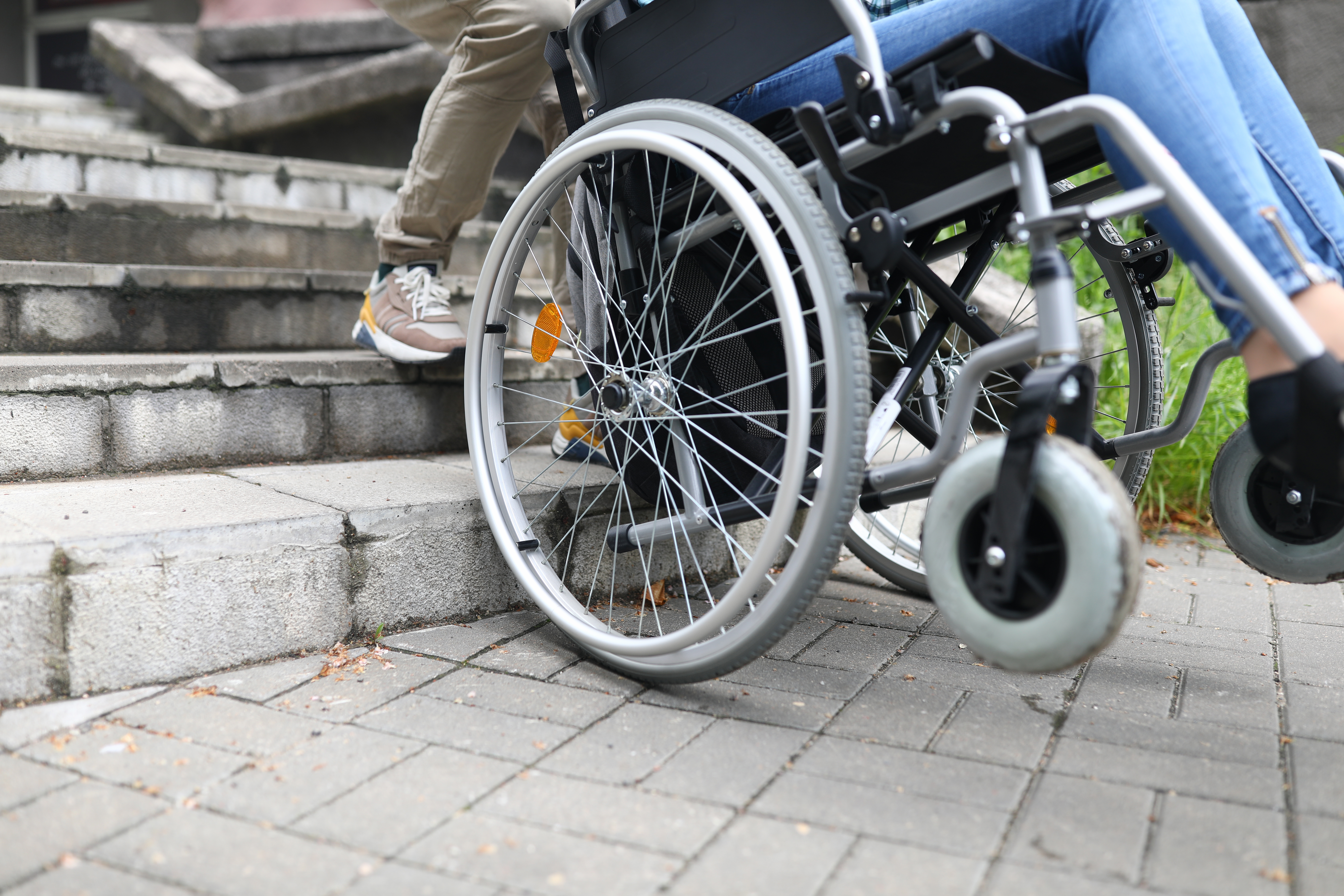 Person helping disabled person in wheelchair climb stone stairs outdoors